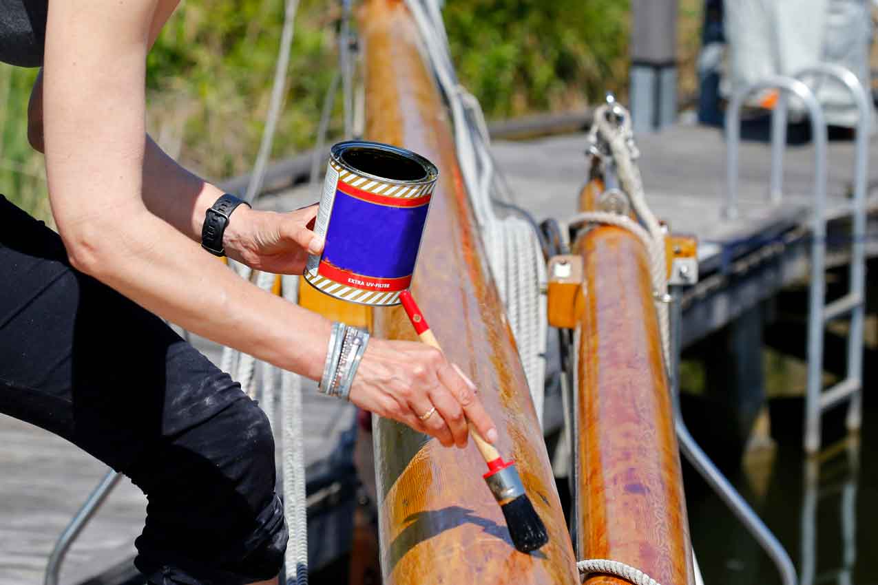 classic-sailing-yacht A young woman varnishing the wooden mast of a classic sailing yacht