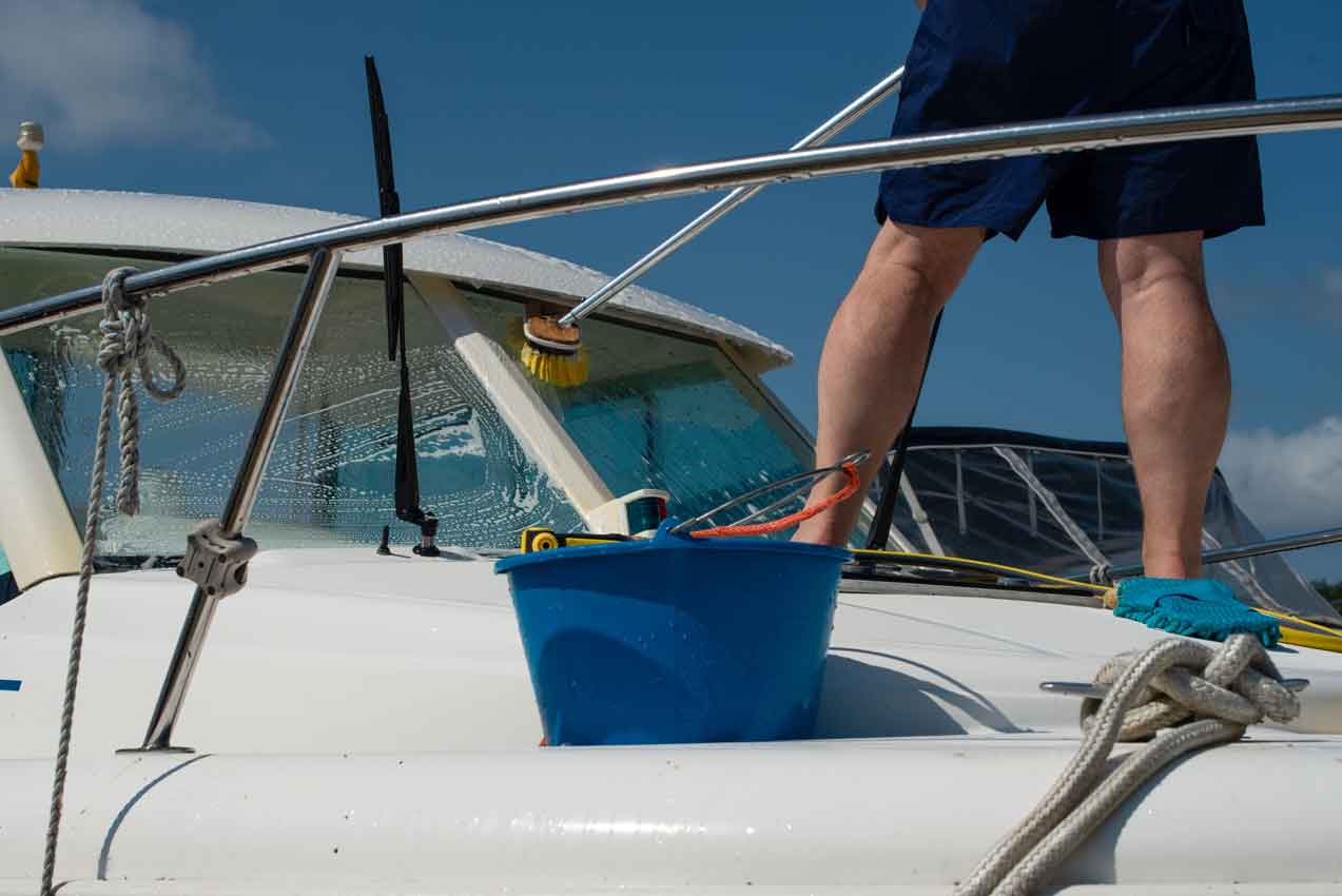 washing-white-boat-with-brush-and-pressure Man washing white boat with brush and pressure water system at marina